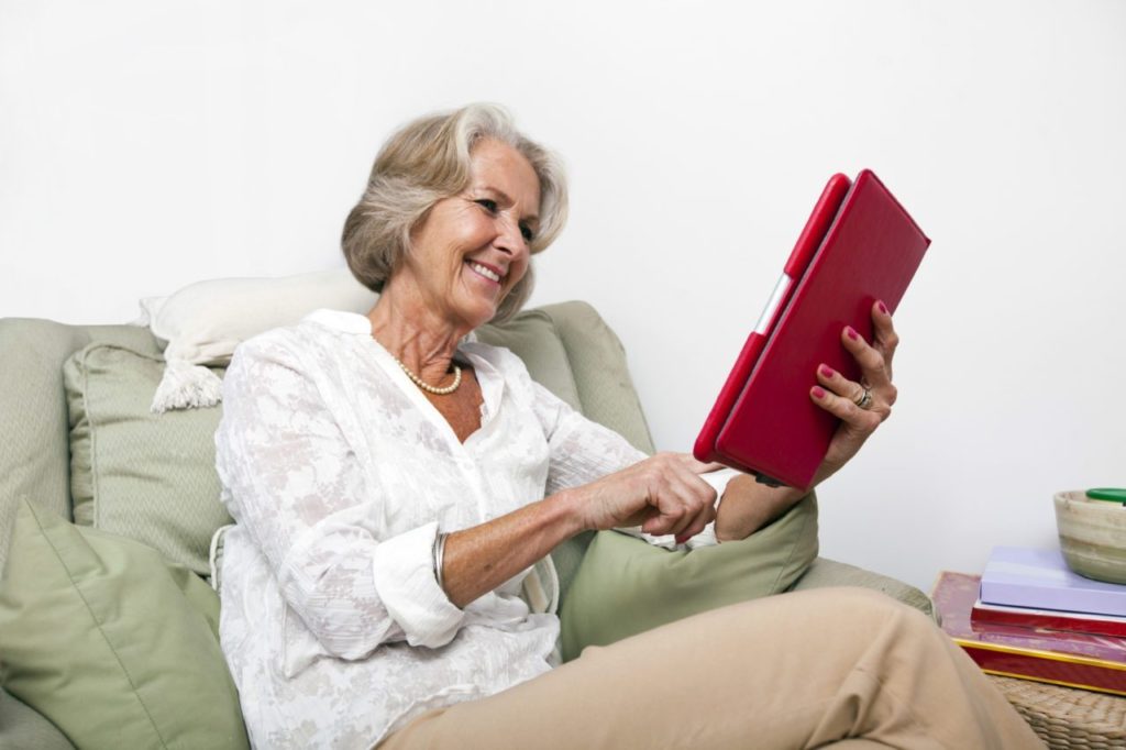 Senior woman using digital tablet on armchair at home