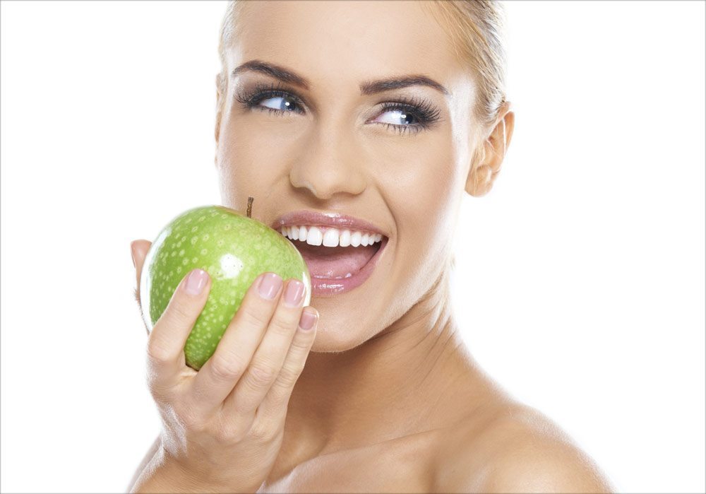 woman smiling while eating a green apple